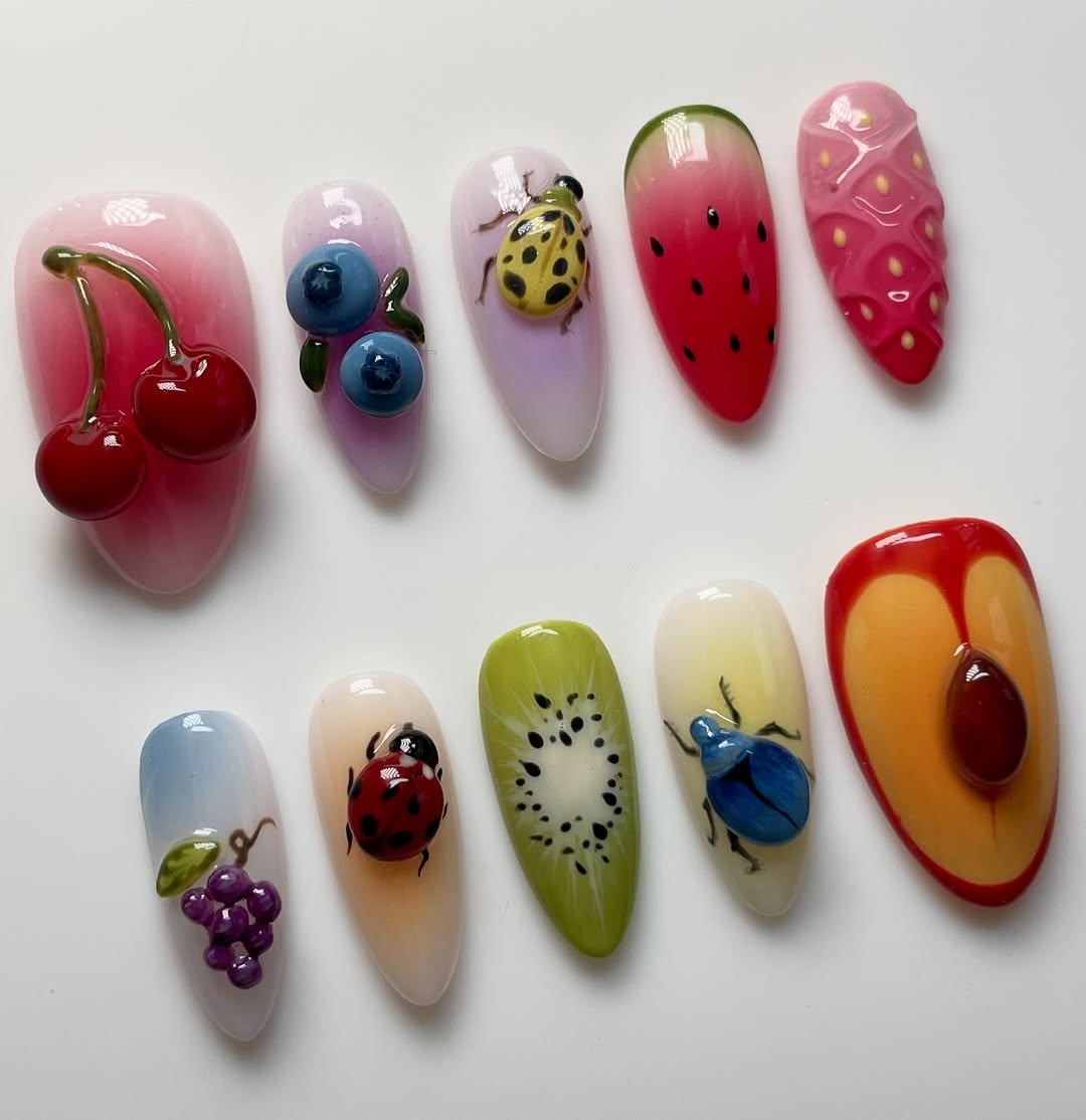 Artistic nail designs resembling fruits and insects on a white background