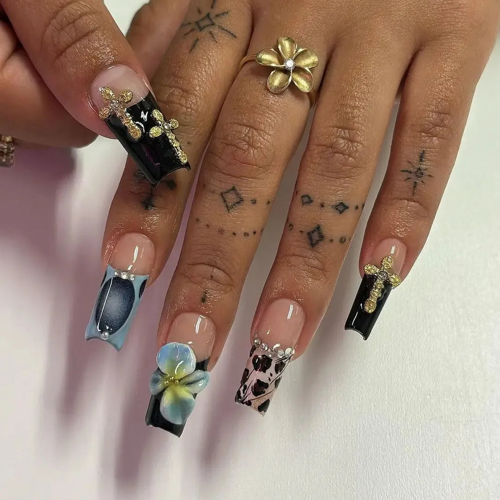 Close-up of a hand with intricately designed nails featuring flowers and patterns on a light background.