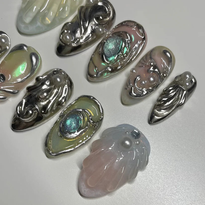 Collection of metallic and gemstone embellishments on a nails on a light gray background