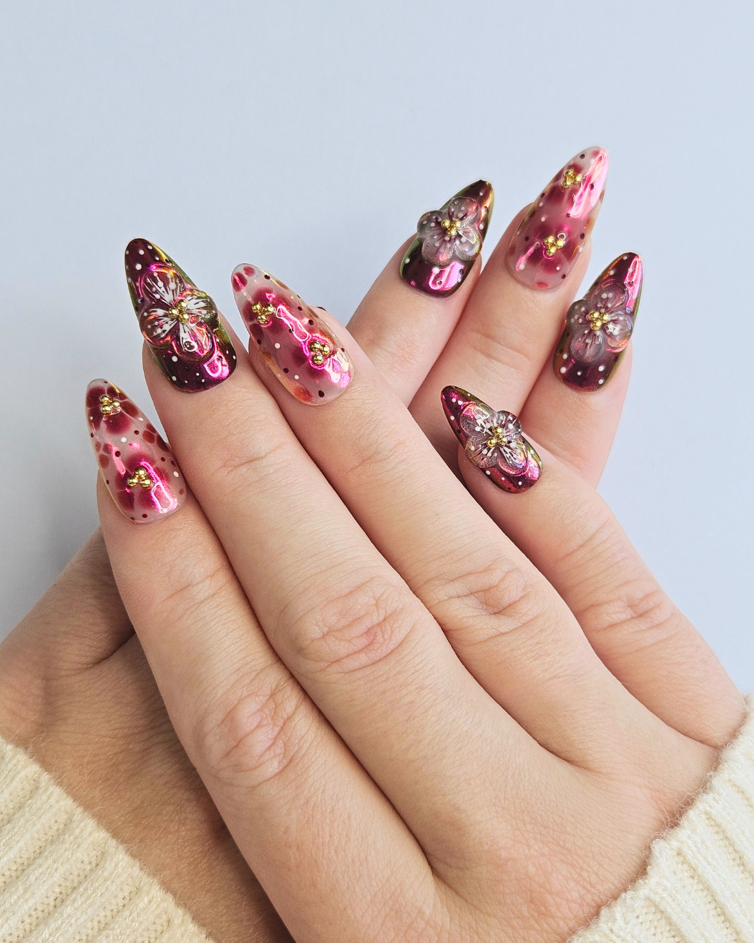 Hand with long, ornate nails featuring pink and gold designs on a light background