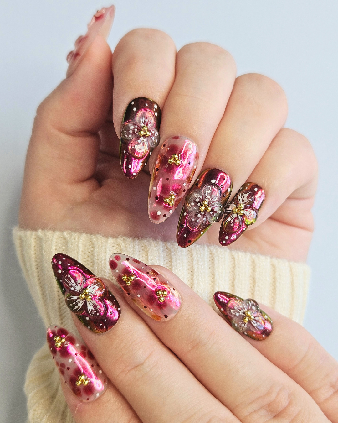 Hand with pink and gold floral nail design on a light background