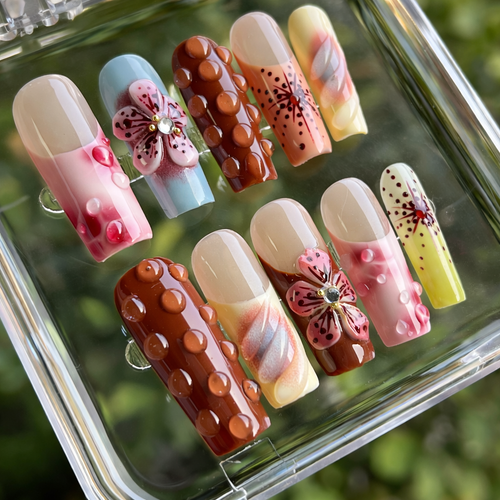 Set of decorative nails with floral and polka dot designs on a clear stand.